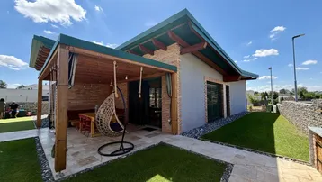 Modernes Haus mit überdachter Terrasse, Sitzbereich und gepflegtem Rasen im Außenbereich.