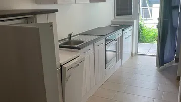 Helle Einbauküche mit weißen Schränken, modernen Geräten und Zugang zu einem Außenbereich.