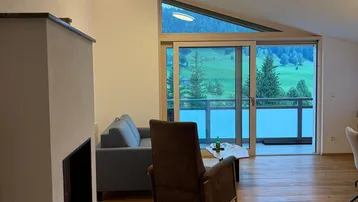 Helles Wohnzimmer mit Holzboden, Kamin und Zugang zu einem Balkon mit Bergblick.