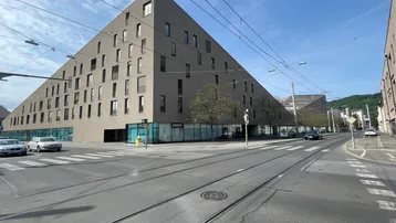 Modernes Gebäude mit ungewöhnlicher, dreieckiger Architektur und vielen Fenstern an einer Stadtstraße.