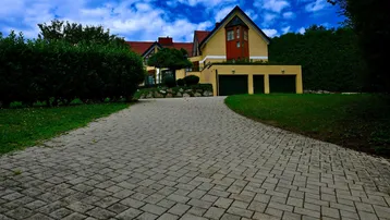 Gepflasterte Auffahrt führt zu einem großen Haus mit integrierter Doppelgarage und gepflegter Gartenanlage.