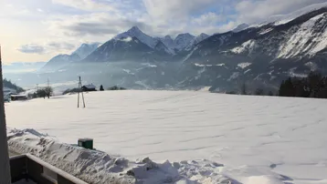 Weite, schneebedeckte Landschaft mit majestätischen Bergen im Hintergrund unter einem Winterhimmel.