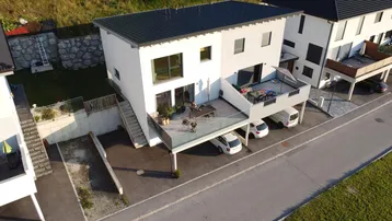 Modernes Einfamilienhaus mit großer Terrasse, Parkplätzen und zeitgenössischer Architektur.