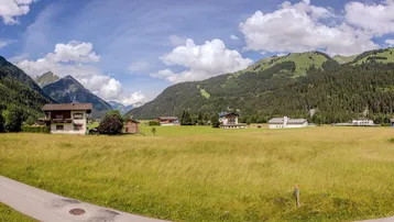 Panoramablick auf grüne Wiesen und majestätische Berge mit traditionellen Häusern in der Ferne.