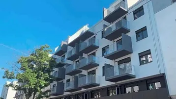Modernes Mehrfamilienhaus mit weißer Fassade und zahlreichen Balkonen unter blauem Himmel.