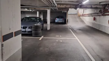 Tiefgarage mit Betonwänden, sichtbaren Rohren und geparkten Fahrzeugen.