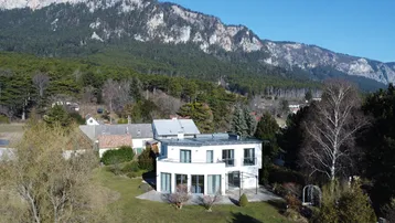 Modernes Wohnhaus mit Flachdach und großem Garten, umgeben von einer malerischen Berglandschaft.