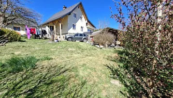 Haus mit großem, grünem Garten auf einem Hanggrundstück unter blauem Himmel.