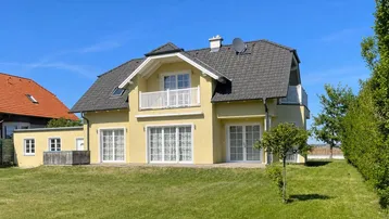 Attraktives gelbes Einfamilienhaus mit dunklem Dach und gepflegtem Rasen im Gartenbereich.