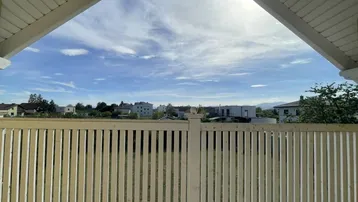 Ausblick von einem Balkon mit Holzgeländer auf die umliegende Wohngegend und Berge.