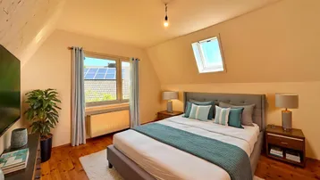 Gemütliches Schlafzimmer im Dachgeschoss mit Holzboden, Dachfenster und Blick auf Solaranlagen.