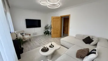 Helles Wohnzimmer mit modernem Sofa, Couchtisch und Fernseher an der Wand.
