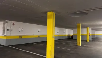 Geräumige Tiefgarage mit markanten gelben Säulen und Betonboden für mehrere Fahrzeuge.