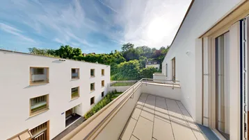 Heller Balkon mit Fliesenboden und Blick auf die grüne Umgebung.