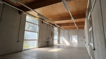 Großer, heller Industrieraum mit hohen Decken, Betonboden und Holzverkleidung an der Decke.