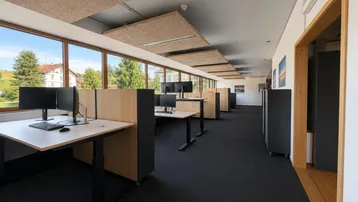 Großes, helles Büro mit mehreren Arbeitsplätzen, großen Fenstern und Blick ins Grüne.
