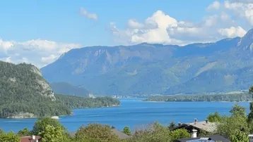 Panoramablick auf einen großen See umgeben von majestätischen Bergen und grünen Hügeln unter blauem Himmel.