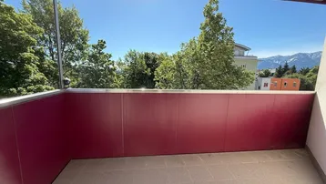 Geräumiger Balkon mit roter Brüstung, Fliesenboden und weitem Blick ins Grüne und auf die Berge.