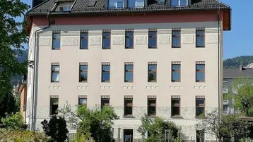 Mehrstöckiges Gebäude mit klassischer Fassade und Dachgauben, umgeben von Grünflächen.
