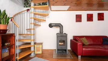 Detailansicht des Holzofens und der Wendeltreppe im Wohnbereich mit rotem Sofa.