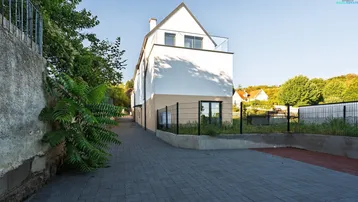 Seitenansicht des modernen Gebäudes mit gepflastertem Weg und Grünflächen.