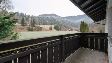 Balkon mit Holzgeländer und weitem Blick über Felder und bewaldete Hügel.