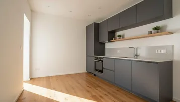 Moderne Küche mit grauen Schränken, Holzboden, integrierten Geräten und viel natürlichem Licht.