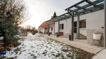 Großer Garten mit Terrasse, Überdachung und Sitzgelegenheiten, teilweise schneebedeckt.