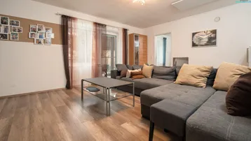 Helles Wohnzimmer mit großem Ecksofa, Laminatboden und Zugang zu einem Balkon oder Terrasse.
