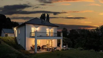 Beleuchtete Villa bei Sonnenuntergang mit gemütlicher Terrasse und weitem Blick in die Natur.