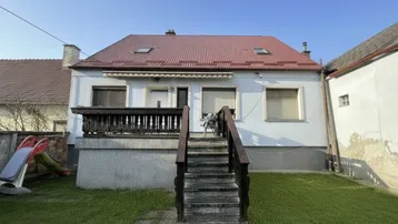 Vorderansicht des Hauses mit rotem Dach, Terrasse und einem kleinen Garten mit Spielbereich.