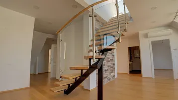 Modernes Wohnzimmer mit offener Treppe, Holzfußboden und viel Tageslicht durch Oberlicht.