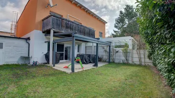 Gepflegter Garten mit Rasenfläche und einer überdachten Terrasse am Haus.