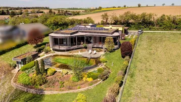 Luftaufnahme des modernen Hauses mit Gründach, Naturpool und weitläufigem Garten in ländlicher Umgebung.