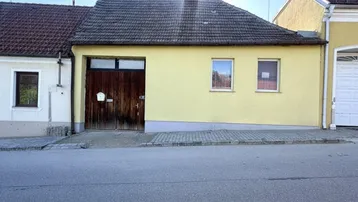 Gelbe Hausfassade mit Holztor und Fenstern direkt an der Straße gelegen.