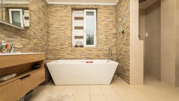 Modernes Badezimmer mit freistehender Badewanne, begehbarer Dusche und Natursteinwänden.