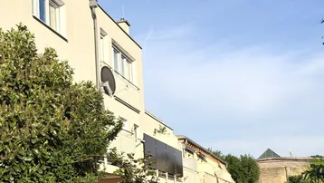 Fassade eines Mehrfamilienhauses mit Balkonen und Satellitenschüssel unter blauem Himmel.