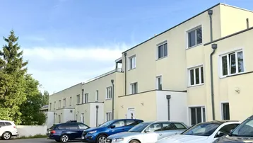 Reihenhäuser mit Parkplätzen davor unter blauem Himmel und grünen Bäumen.