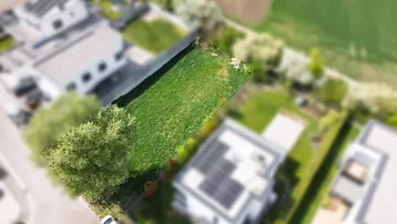 Luftaufnahme eines grünen Grundstücks umgeben von modernen Häusern und Feldern.