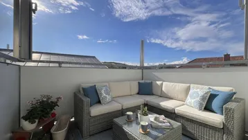 Gemütlicher Balkon mit Loungemöbeln und weitem Blick unter blauem Himmel.