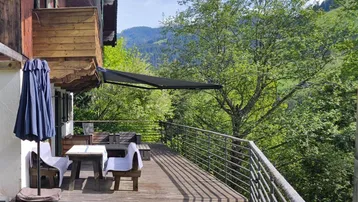 Geräumige Holzterrasse mit Sitzgelegenheiten, Sonnenschirm und weitem Blick auf die grüne Berglandschaft.