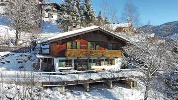 Traditionelles Chalet in verschneiter Berglandschaft mit Holzbalkon und grünen Fensterläden.