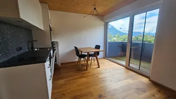 Moderne Küche mit Essbereich, Holzboden und Zugang zum Balkon mit Bergblick.