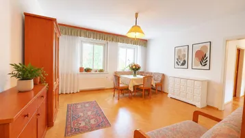 Helles Wohn- und Esszimmer mit Parkettboden, zwei Fenstern und traditionellen Möbeln.