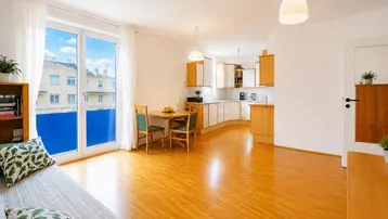 Helles Wohn- und Esszimmer mit offener Küche, Parkettboden und Zugang zum Balkon.
