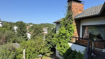 Balkon mit Blick ins Grüne und auf die umliegende Wohngegend unter blauem Himmel.