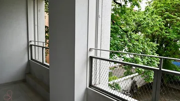 Schmaler Balkon mit modernen Metallgeländern und Blick auf grüne Bäume und die Straße.