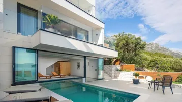 Moderne Villa mit Infinity-Pool, Sonnenliegen und Meerblick, umgeben von üppiger Natur und Bergen.