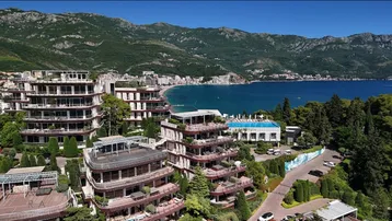 Panoramablick auf die luxuriöse Wohnanlage mit Pool, Strand und majestätischer Bergkulisse.