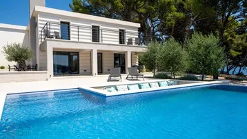 Moderne Villa mit großem Poolbereich und Meerblick unter blauem Himmel.